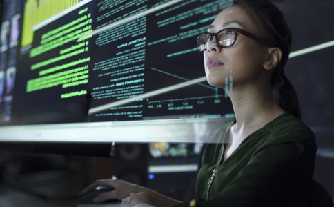 Stock photo of a young Asian woman looking at see through data whilst seated in a dark office