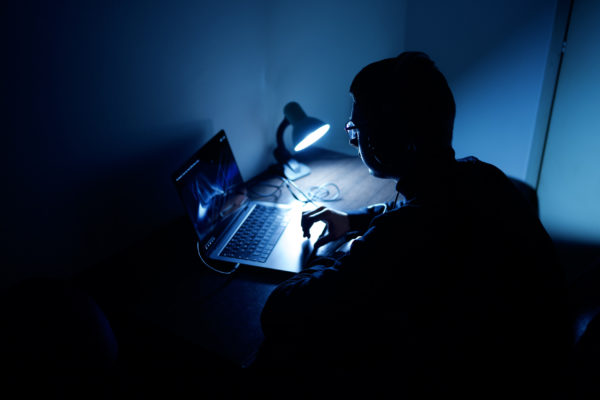 Young freelancer in his room, working at home on laptop in dark atmosphere