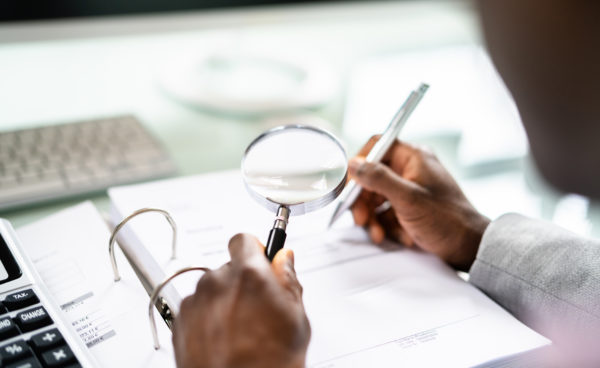 Auditor Or Fraud Investigator Looking At Tax Document Using Magnifying Glass